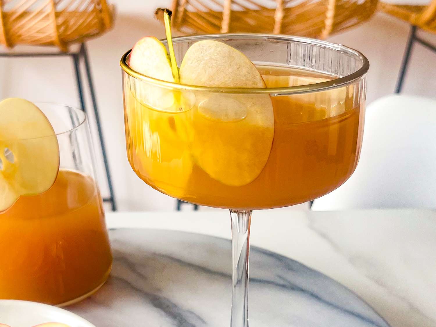 A stemmed glass filled with a goldenhued beverage garnished with apple slices on a marble surface