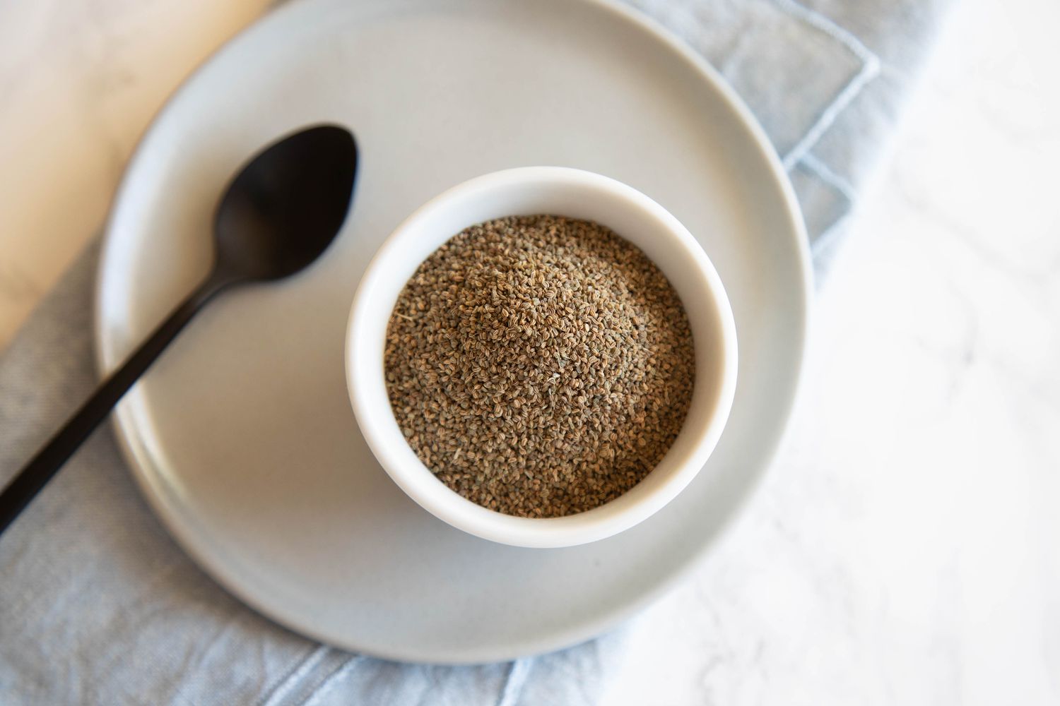 White bowl full of celery seed spice next to black spoon