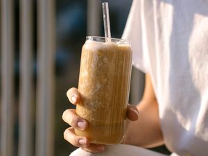 A hand holding a tall glass filled with a smoothie a straw in the drink