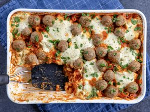 Baked pasta casserole topped with meatballs and cheese a portion removed showing layers of pasta and sauce