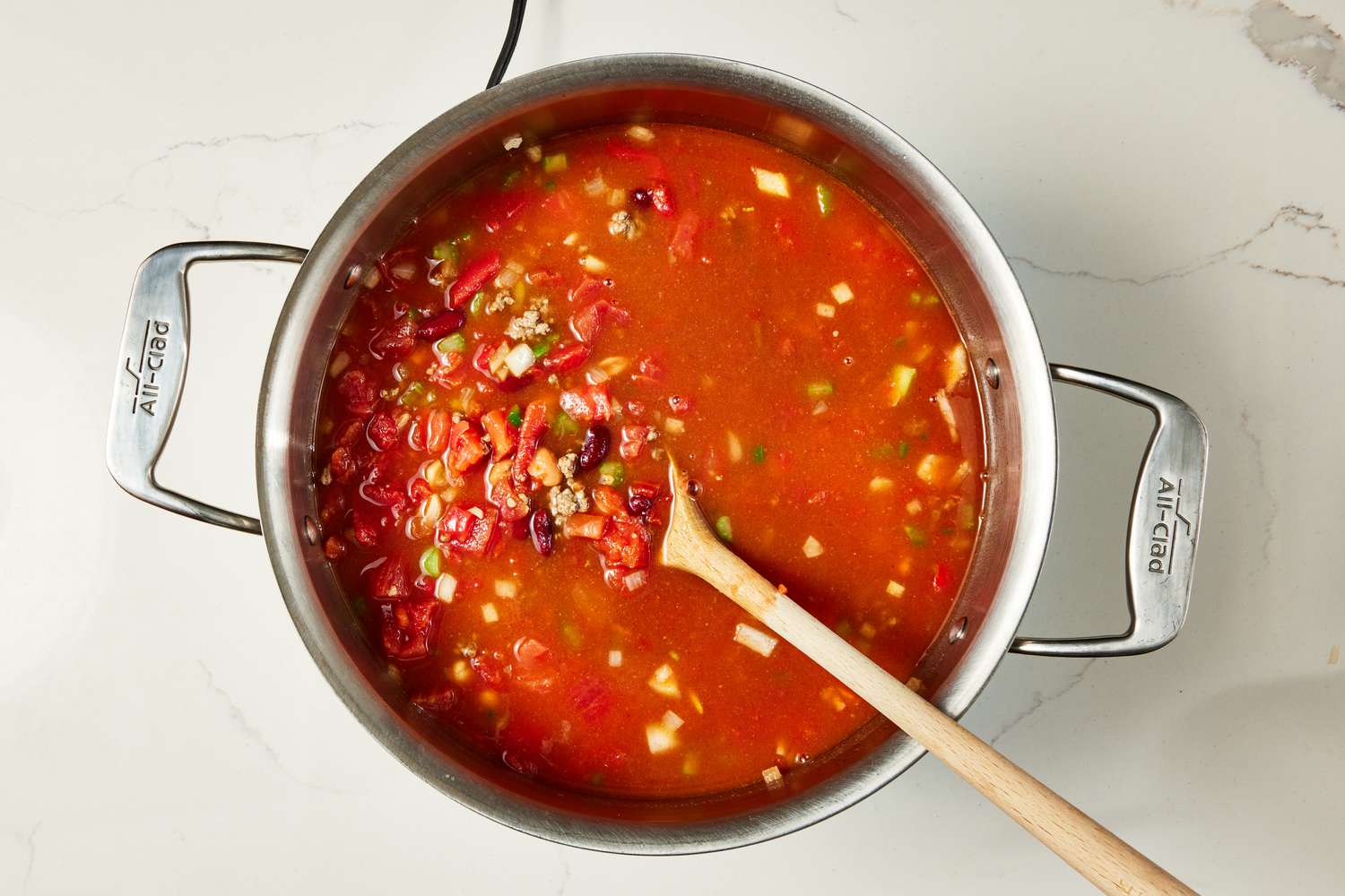 Beans and the liquid ingredients added to the pot (some of the ingredients slightly lifted using a wooden spoon) for copycat Wendy's chili recipe
