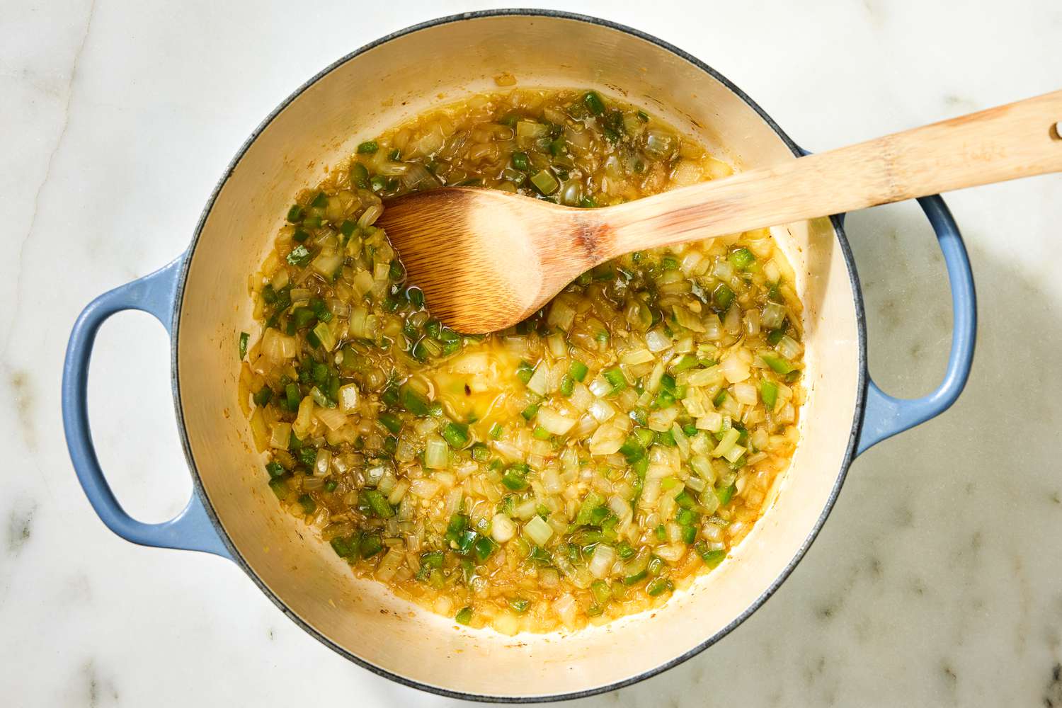 Overhead view of a blue dutch oven after adding the onions, bell pepper, garlic, and salt for Country Captain Chicken recipe