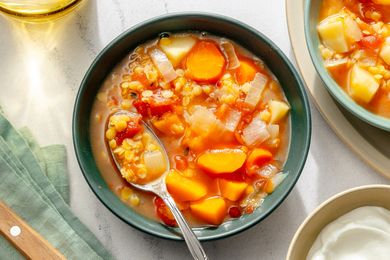 A bowl of slowcooked red lentil soup with vegetables and a spoon