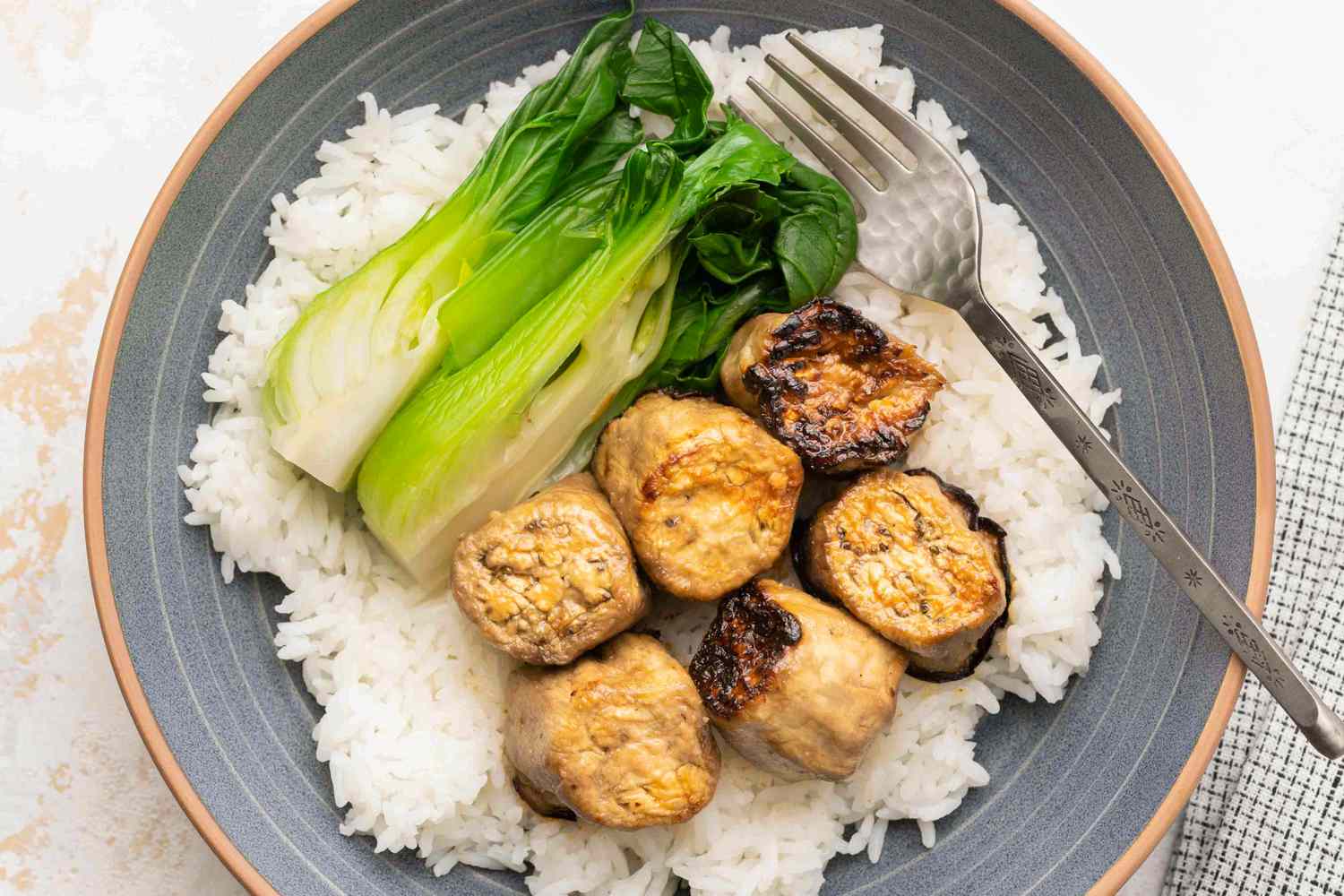 Miso-Glazed Eggplant on a bed of rice with baby bok choy on a plate with a fork