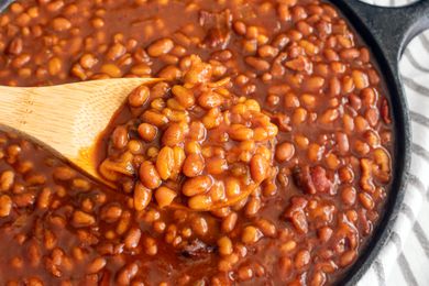 Baked beans in a cast iron skillet with a wooden spoon