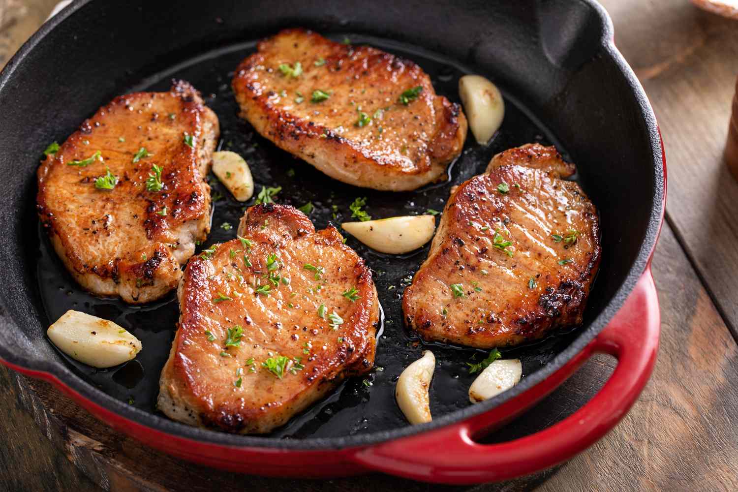 Four pork chops frying in a castiron pan with garlic cloves