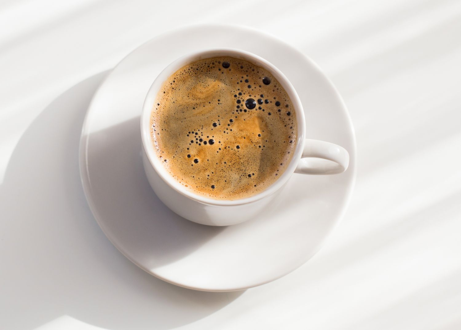 Overhead view of a cup of coffee and a white saucer on a white background