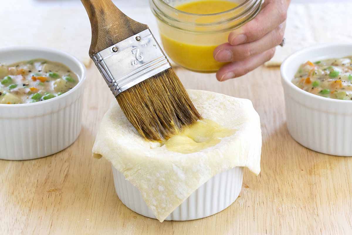 Puff pastry sheets being brushed with egg wash on top vegetarian pot pies.