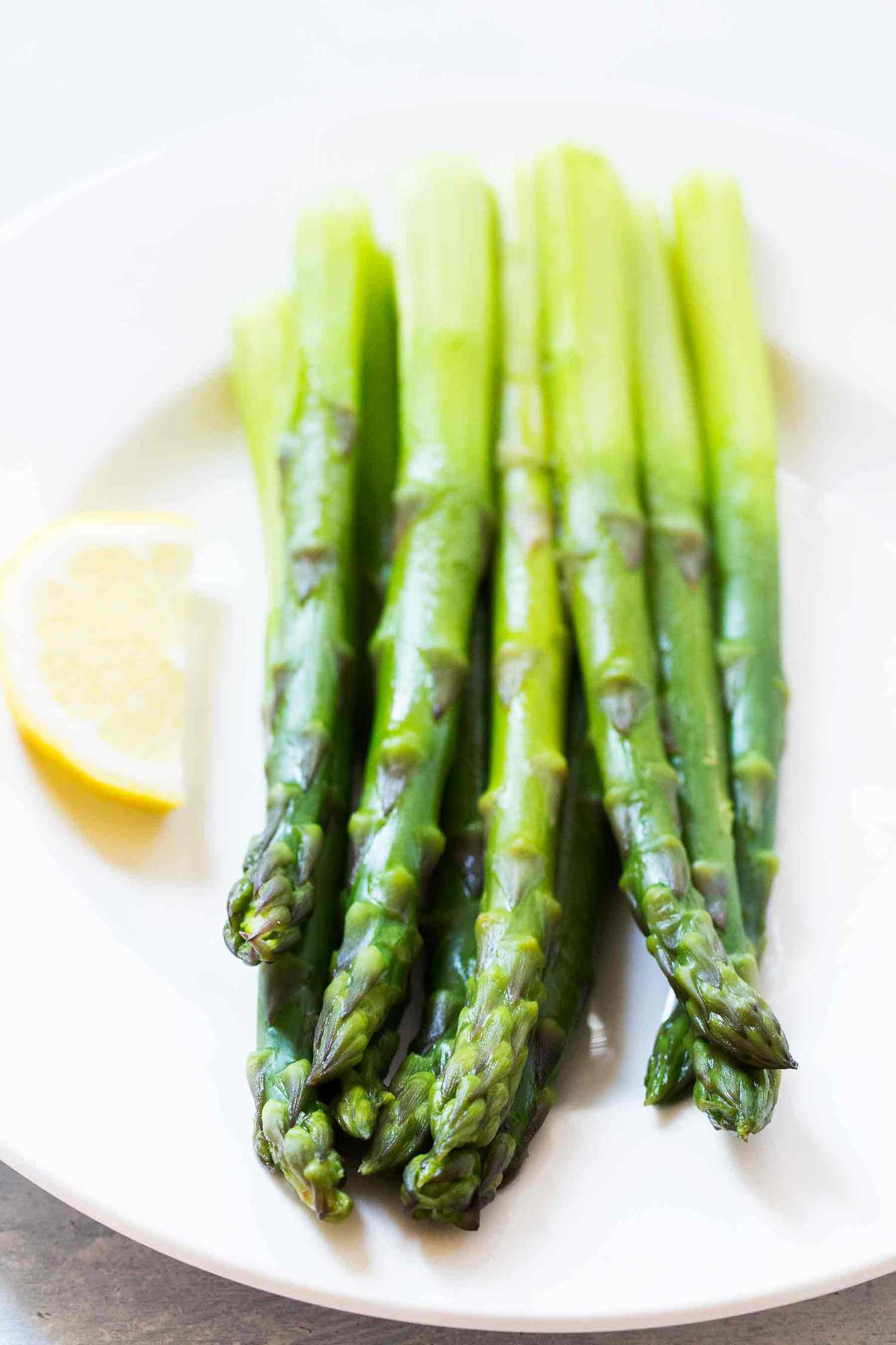 stovetop asparagus on a white plate with lemon on the side