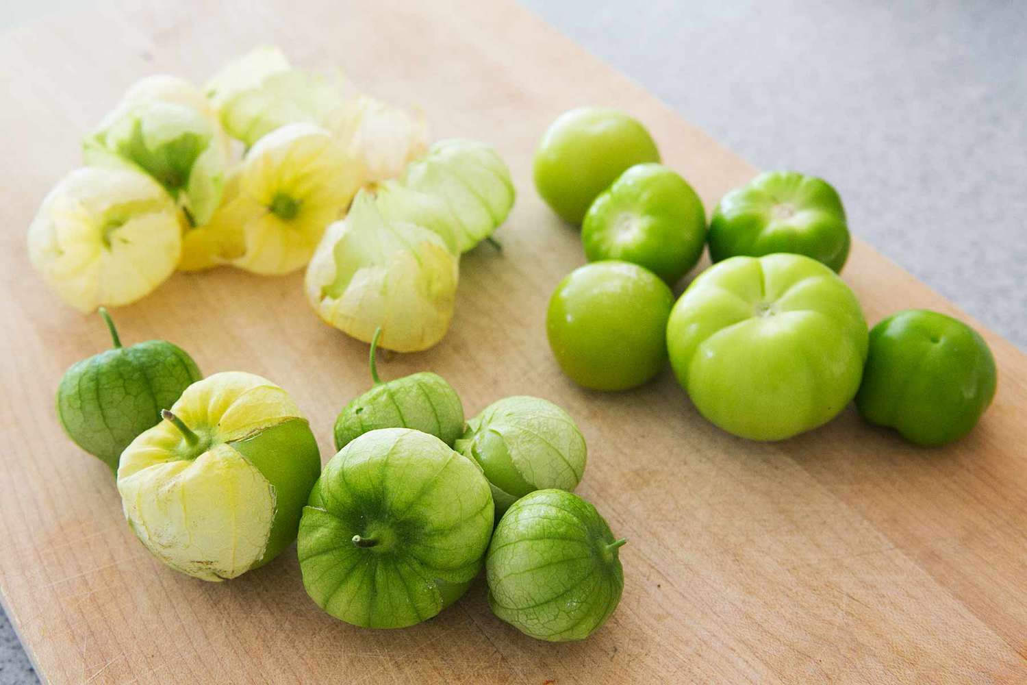 Tomatillos resting on a cutting board and in the process of being peeled 