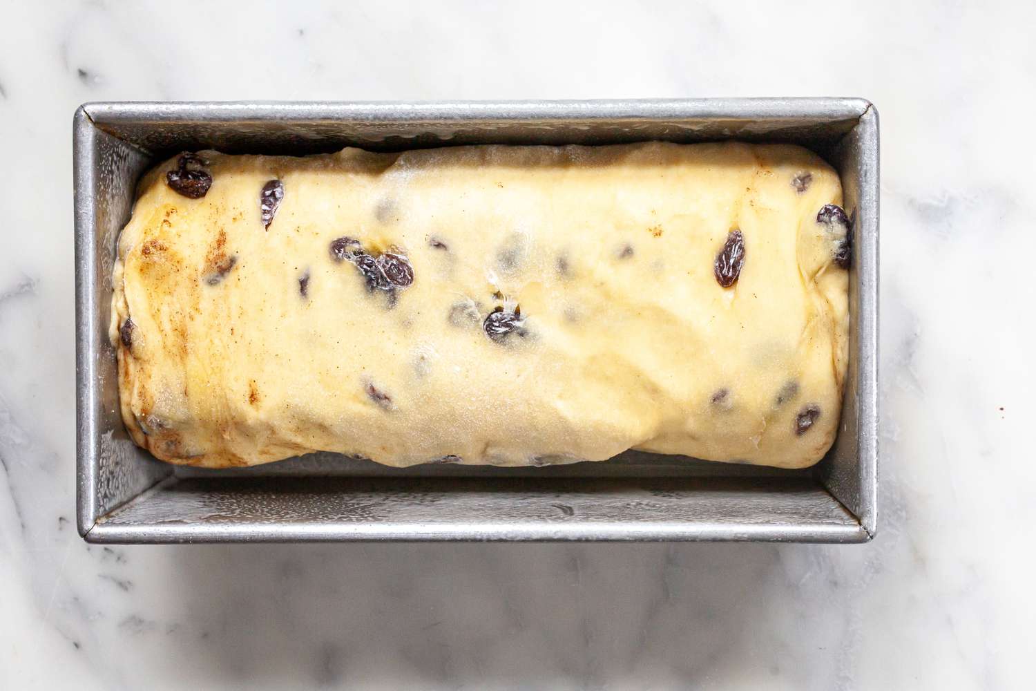 Cinnamon Swirl Raisin Brioche Loaf Resting in a Baking Pan 