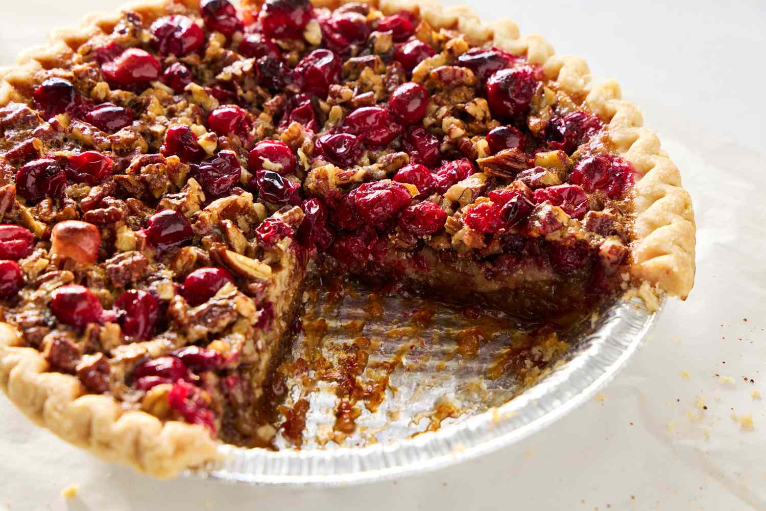Cranberry pecan pie with a slice removed displayed on a clear pie tin