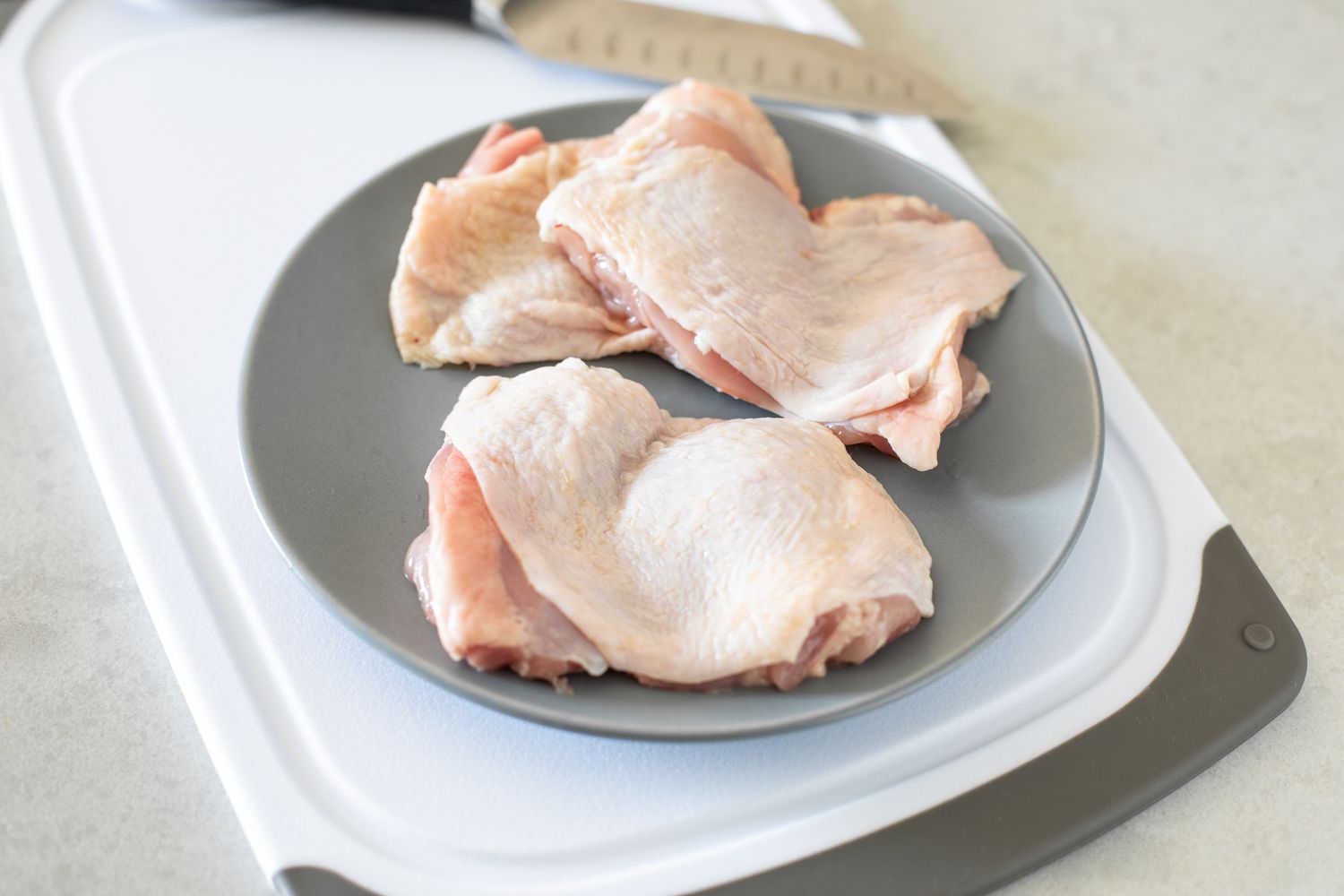 Plate of Boneless Chicken Thighs on a Cutting Board and on the Counter Next to It, a Knife