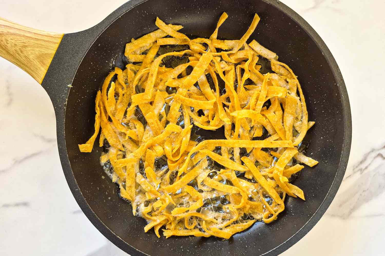 Frying pan with thinly sliced fried tortilla strips on a marble counter