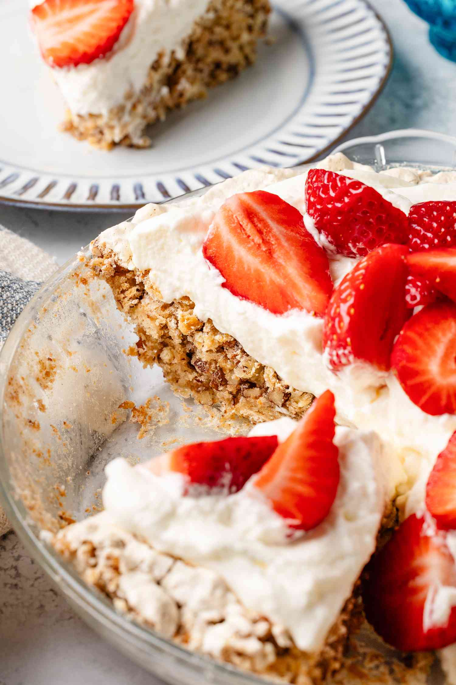 soda cracker pie topped with whipped cream and fresh strawberries in a baking pan (with some slices cut out) and in the background, a slice on a small plate