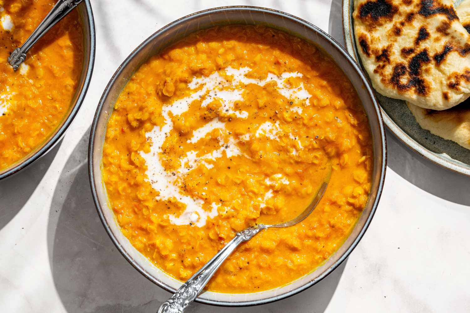 Coconut Lentil Soup garnished with yogurt in a bowl with a spoon, naan on the side