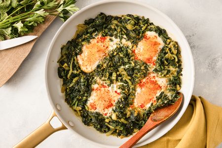 A pan of Nargesi a Persian dish with eggs cooked atop seasoned sauted greens displayed on a countertop next to utensils