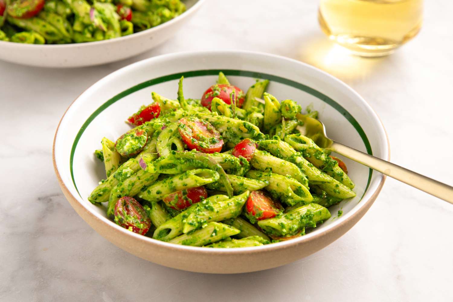 A bowl of pasta with spinach and feta garnished with cherry tomatoes fork beside