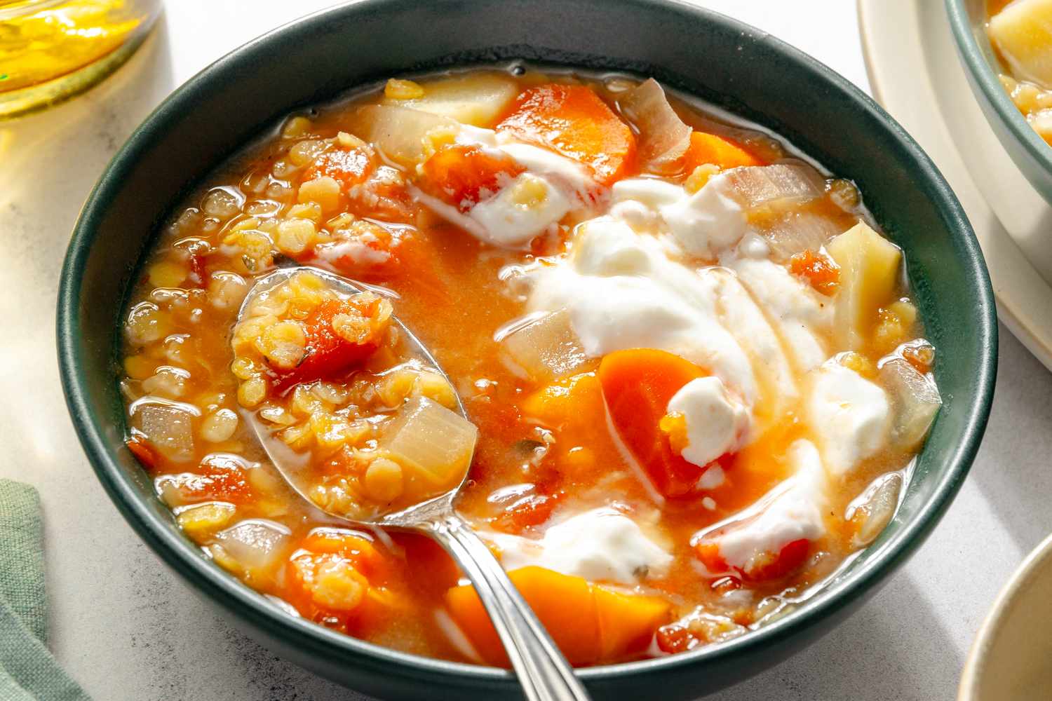 Bowl of red lentil soup with carrots potatoes and a spoon inside topped with a dollop of creamy garnish