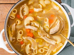 A pot of macaroni chicken sopas (Filipino chicken noodle soup), with a golden serving spoon scooping some soup out