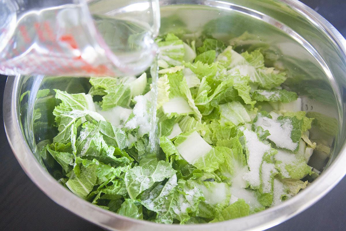 Water being added to the bowl with cabbage and salt to show how to make kimchi.