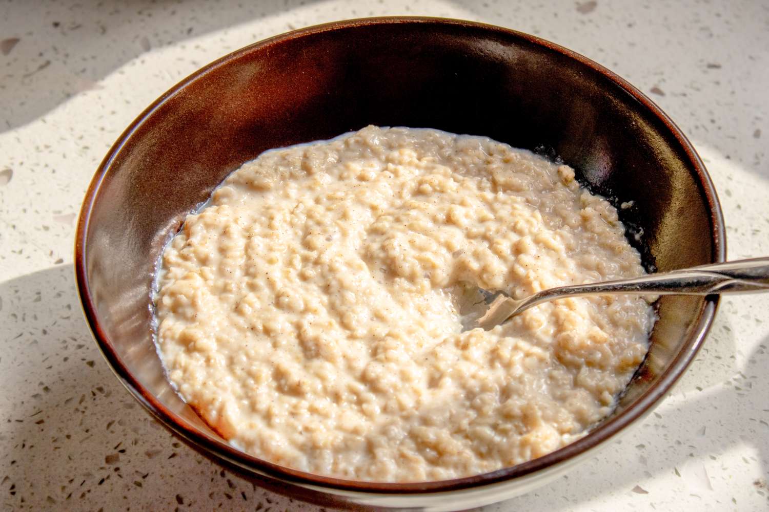 A bowl of oatmeal with a spoon on a speckled surface