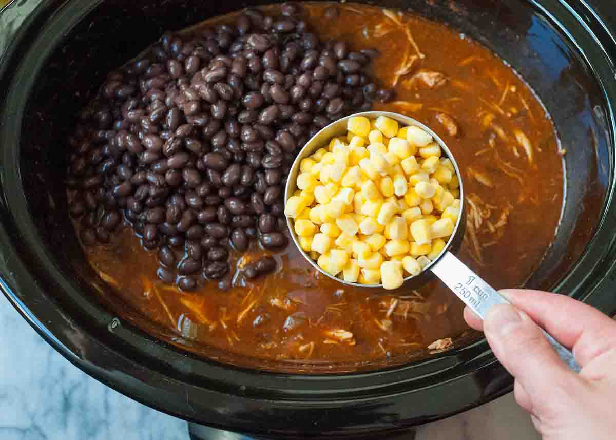 Adding the beans and corn to the slow cooker chicken chili