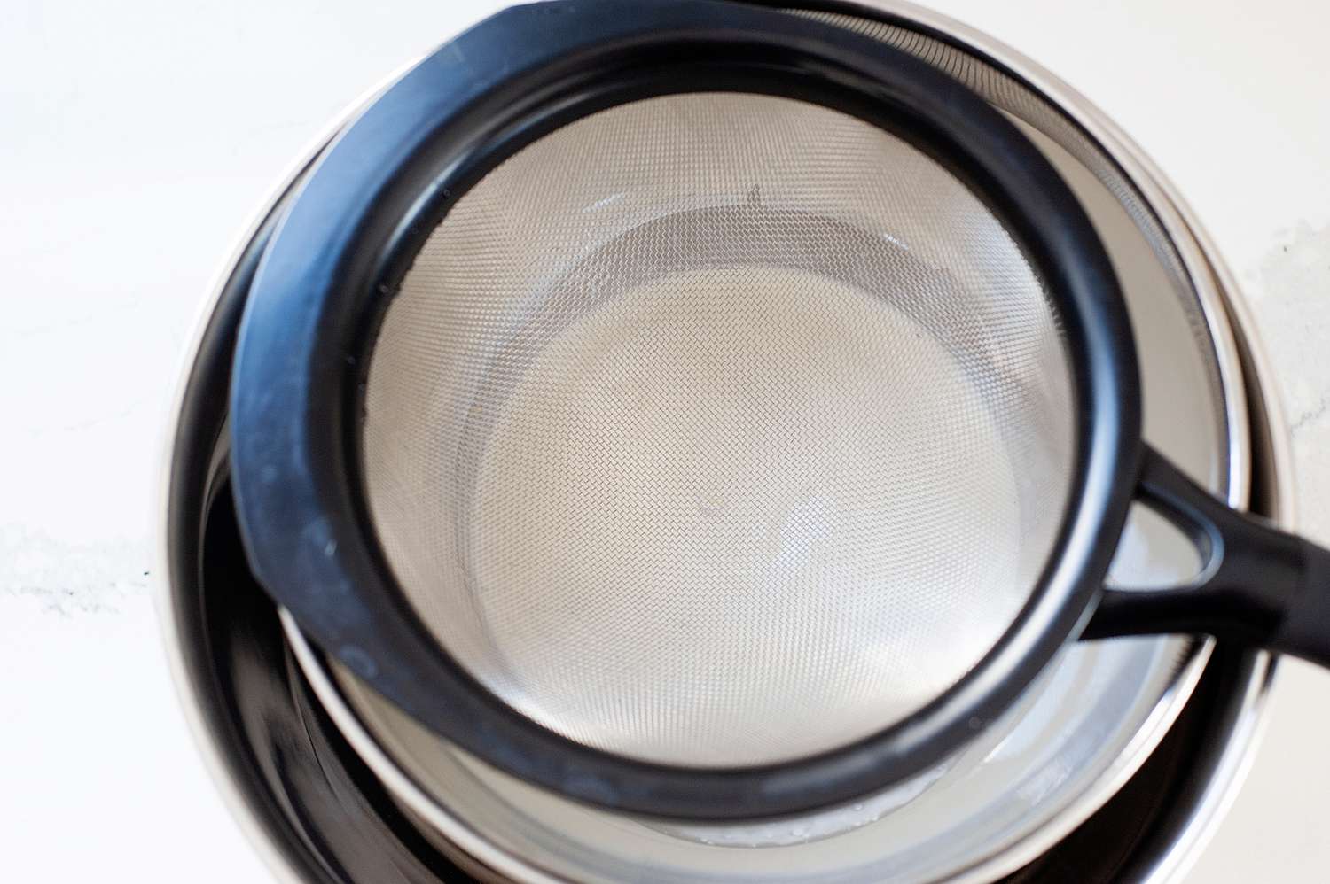 Straining the base of cinnamon ice cream into a metal bowl.