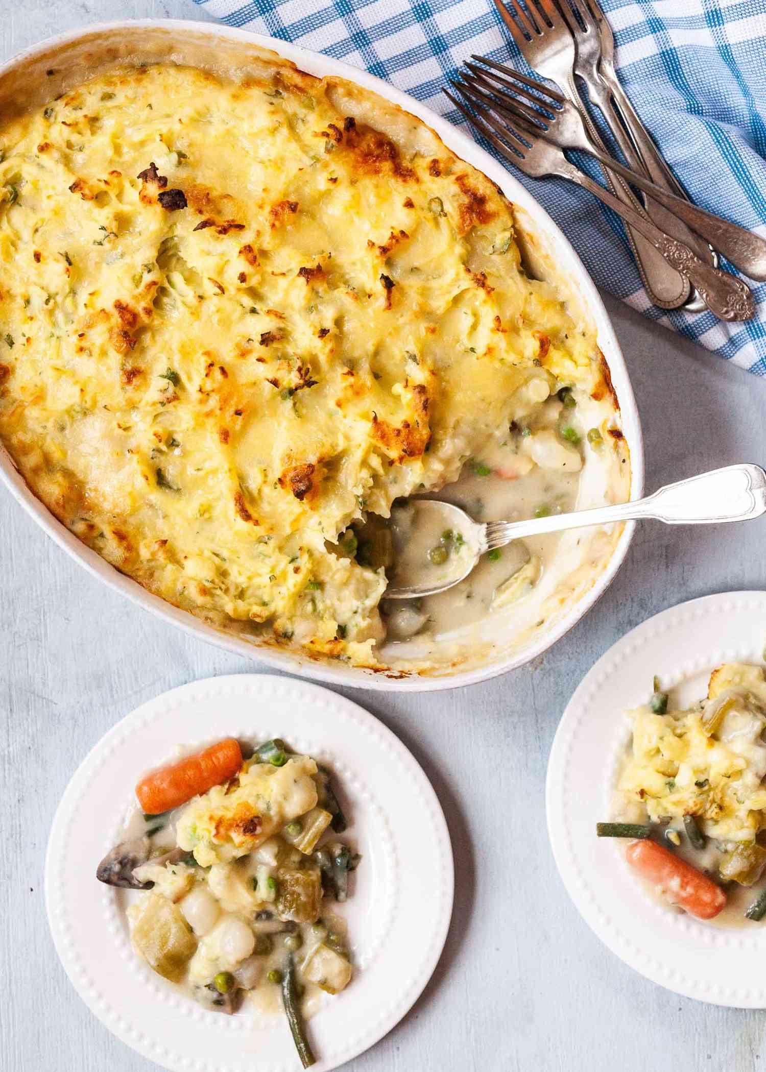 Vegetarian Shepherd’s Pie Recipe - white casserole dish wtih shepherds pie, a spoon and two white plates with sheperds pie served upon them.