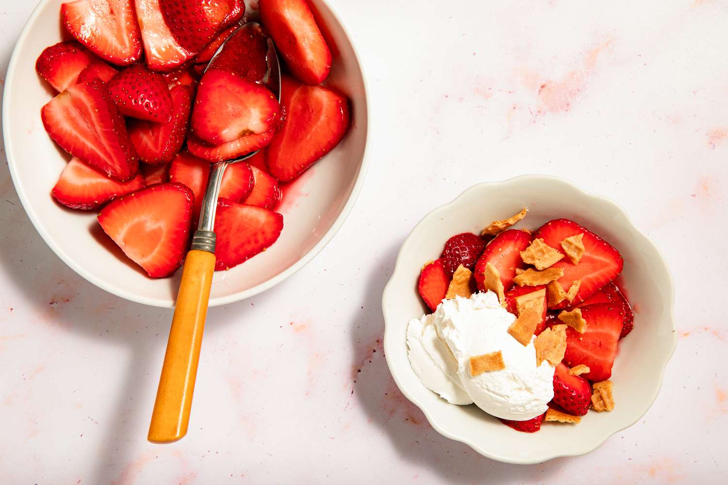 Sliced strawberries in a bowl with a dessert serving topped with cream and crumbled topping nearby