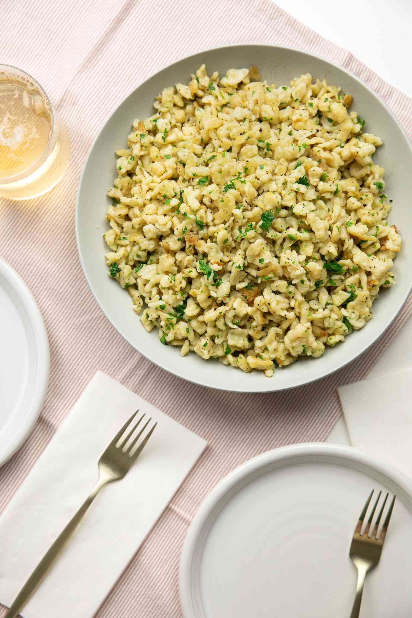 Bowl of Homemade Spaetzle (Spätzle) at a Table Setting with Two Drinks, Two Plates, and Forks on a Table Napkin