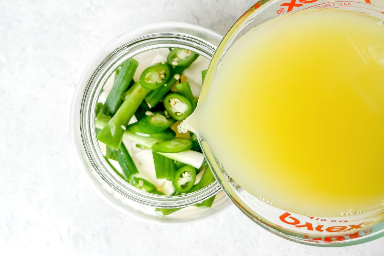 Strained Liquid in a Pyrex Measuring Cup Poured Into a Jar With Dongchimi Ingredients for Naengmyeon (Korean Cold Noodle Soup)