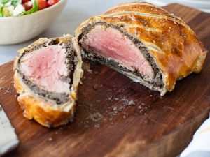 Beef Wellington Sliced in Half on a Cutting Board Next to a Bowl of Side Salad