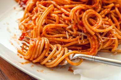 pasta (in marinara sauce) wrapped around a fork on a plate with more sauced pasta