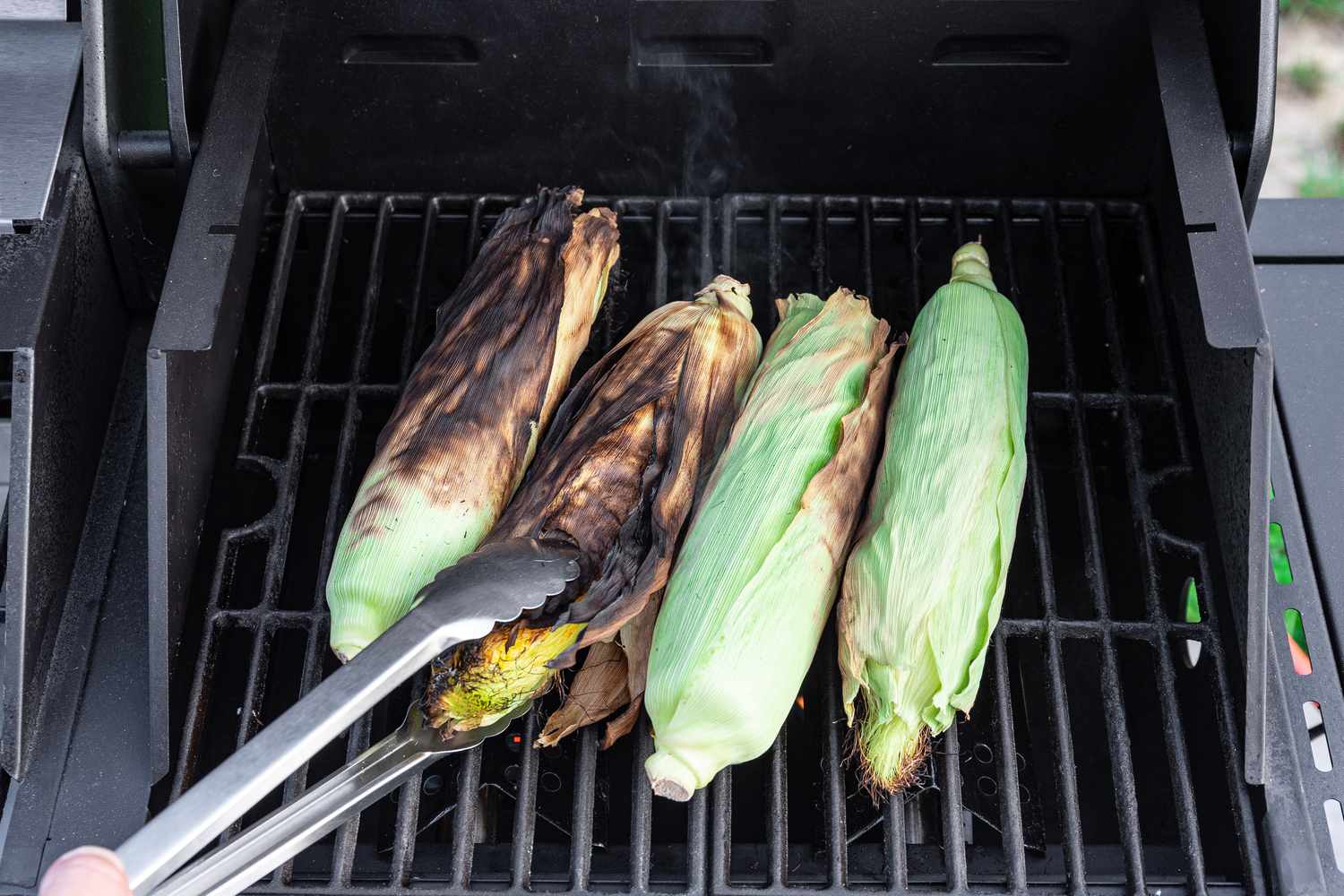 Grilling Corn on the Cob (Partially Charred) and Flipped Using Tongs 