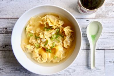Overhead view of a bowl of pork and ginger wontons in chicken soup.