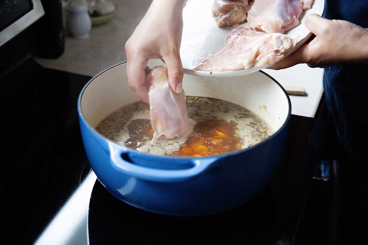 Raw chicken thighs being placed into simmering stock.