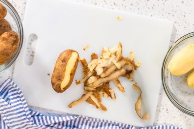 Potato peel and a half peeled potato on a white cutting board