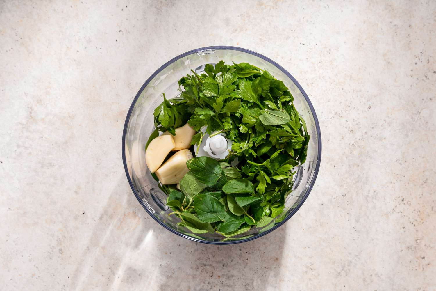 An open food processor with unchopped garlic and herbs