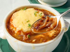 French onion soup topped with melted cheese and garnished with herbs served in a white bowl on a saucer