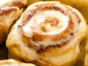 A closeup of a glazed cinnamon roll with visible swirls of cinnamon filling and icing