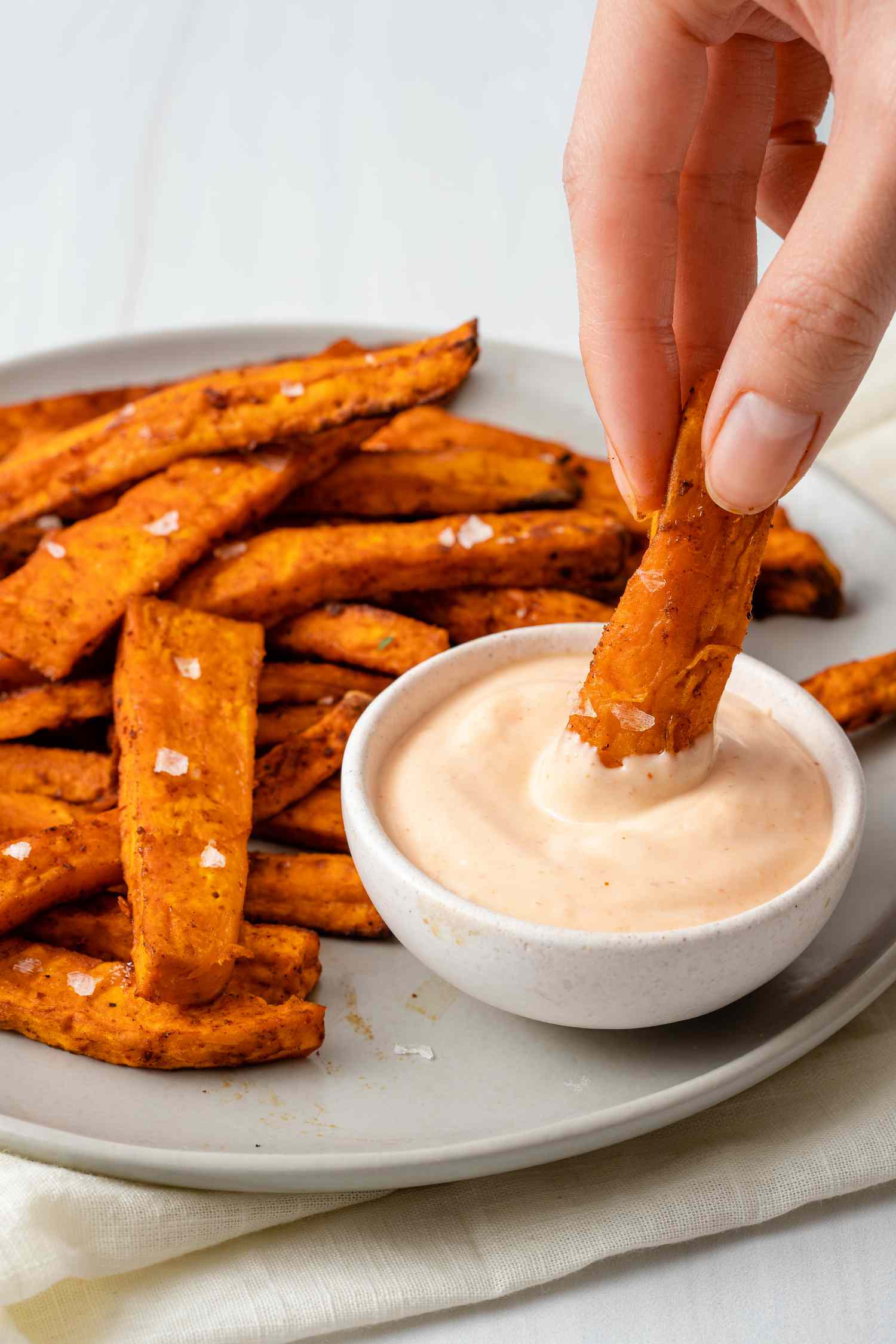 A platter of sweet potato fries with a person dipping one in a sauce.