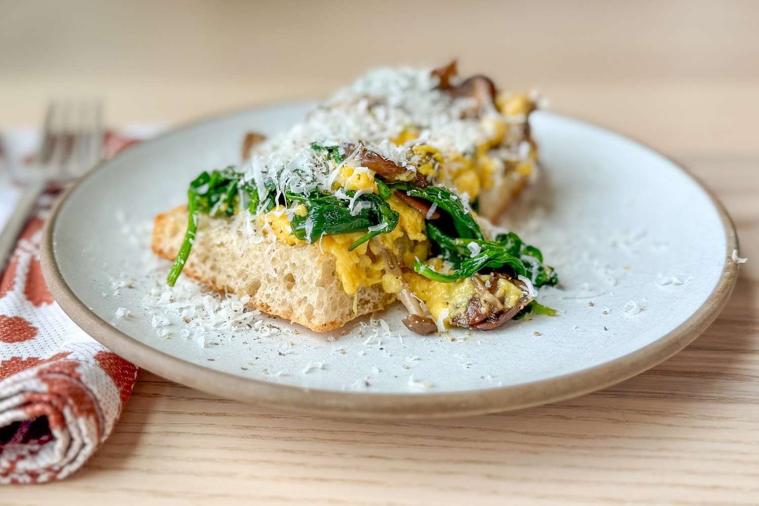 Side view of a plate with a piece of bread topped with scrambled eggs mixed with spinach and mushroom, topped with cheese