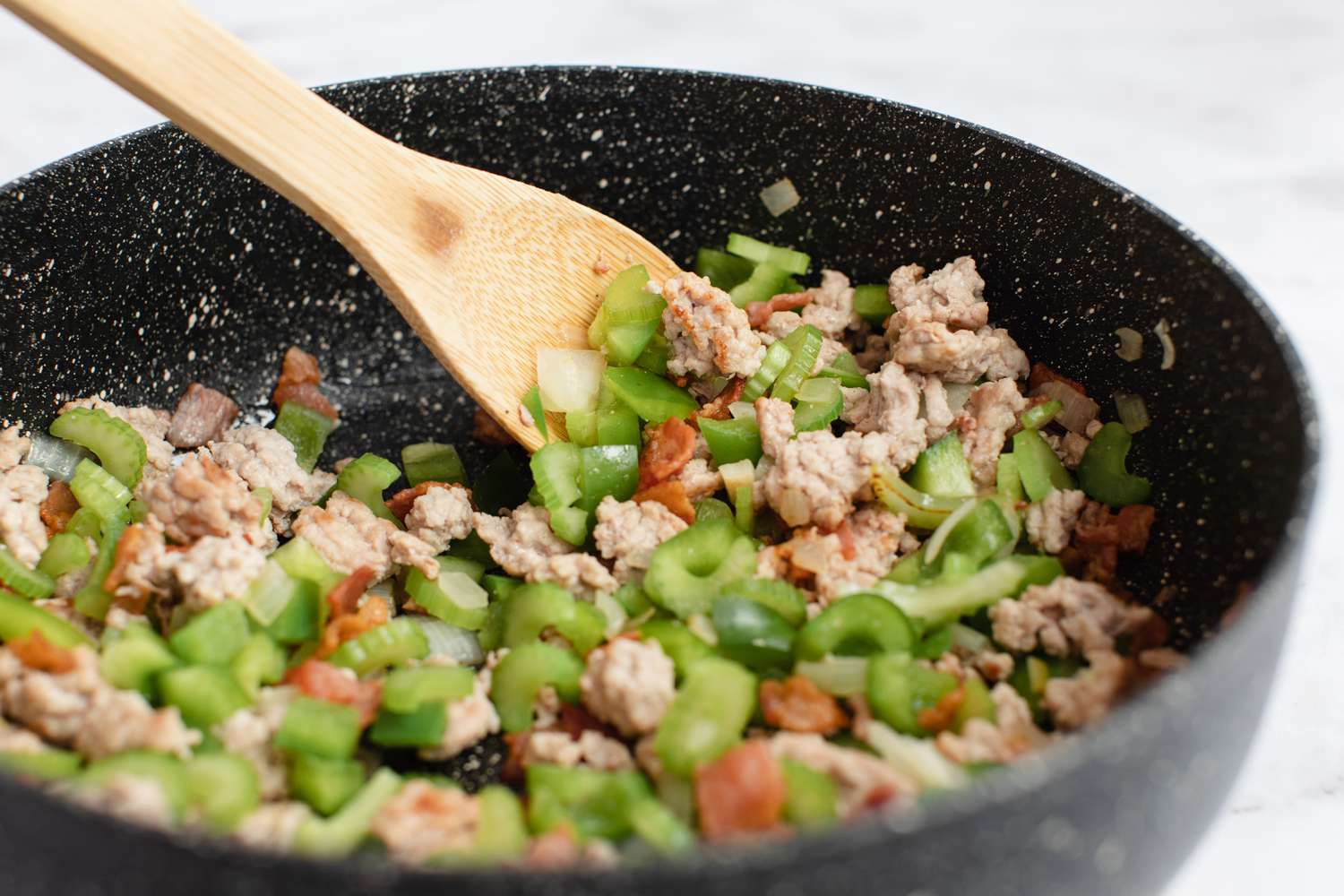 Adding vegetables to a skillet to make Cajun dirty rice.