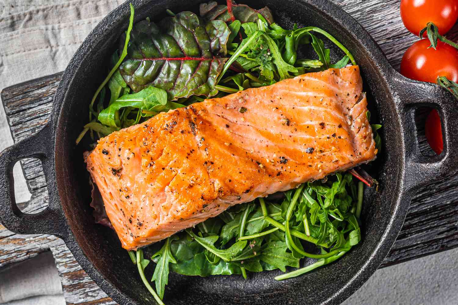 cooked salmon fillet on a bed of mixed greens, all in a small cast iron skillet