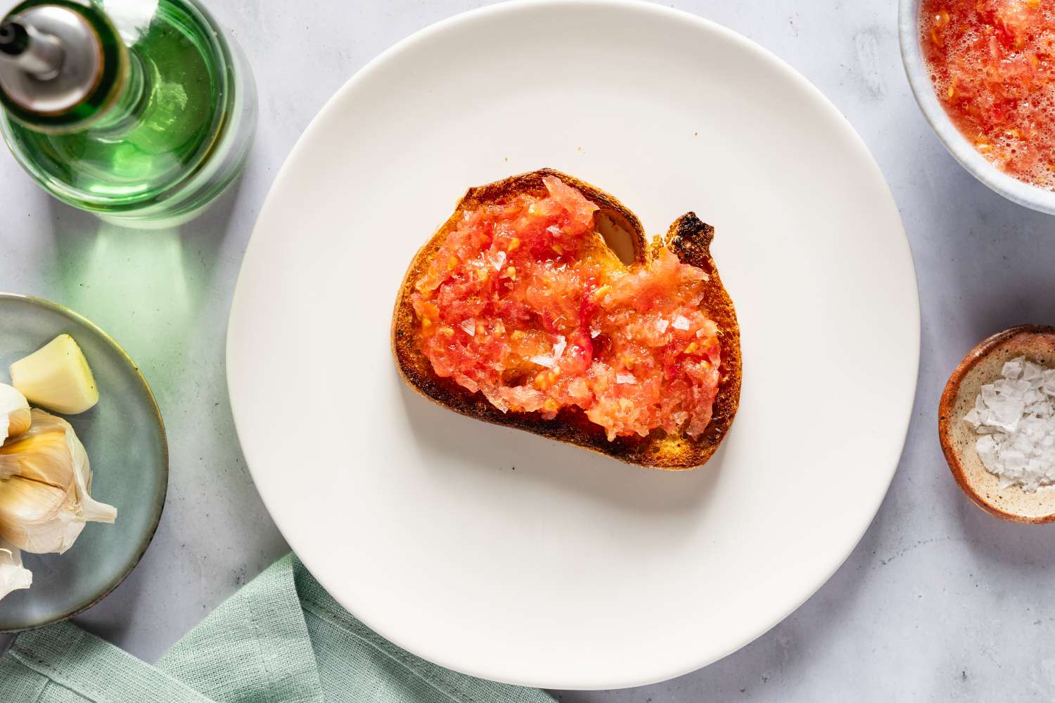 A plate with a slice of bread topped with crushed tomato surrounded by kitchen items