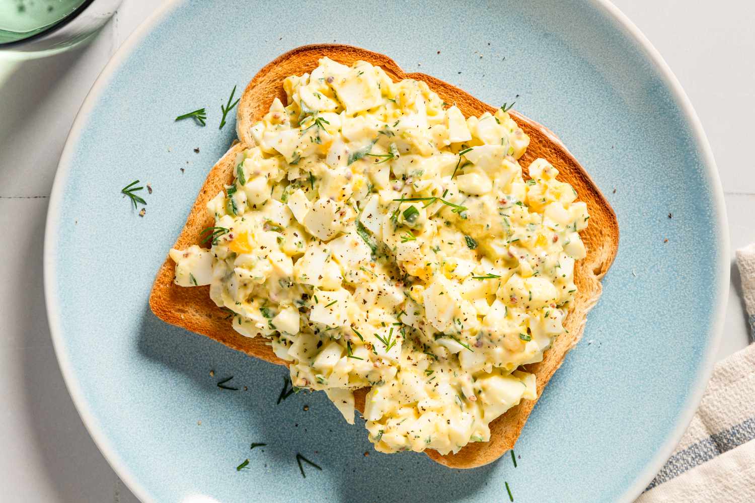 Overhead view of a dill egg salad on a piece of toast on small blue plate