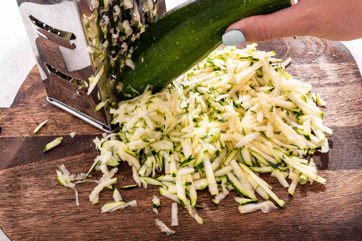 Zucchini Grated Using a Box Grater Over a Wood Cutting Board for Zucchini Butter Recipe