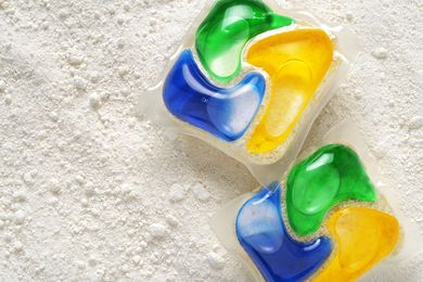 Close up of two multicolored dishwasher detergent pods on a background of dish detergent powder