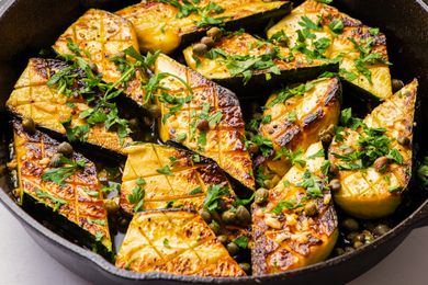 Sautéed zucchini pieces in a skillet garnished with herbs and capers